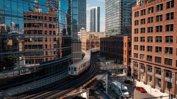 High view of Chicago train on elevated rail in downtown with reflective glass building on left and brick building on right.