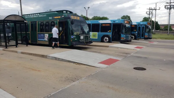 Three green and teal buses at a multi-lane bus station.