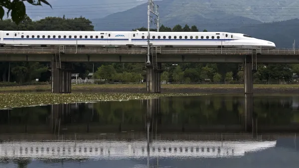 White Shinkansen high-speed rail train passing on bridge over pond in Japan.