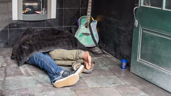 Two people sleeping under a blanket on the street in New Orleans next to a guitar