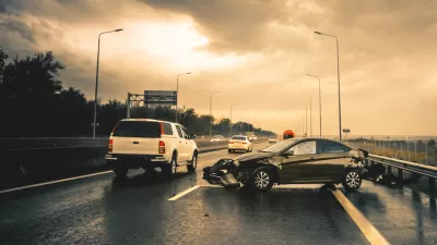 Small black car with mangled bumper sitting sideways on an asphalt road