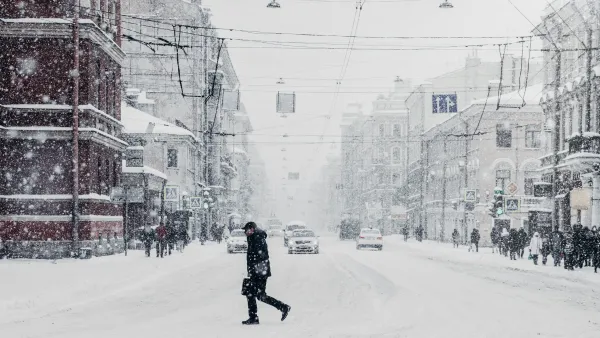 Man walking through snow in city with snow falling.