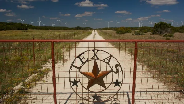 Metal gate with Texas logo and star with wide open field with white wind turbines behind it.