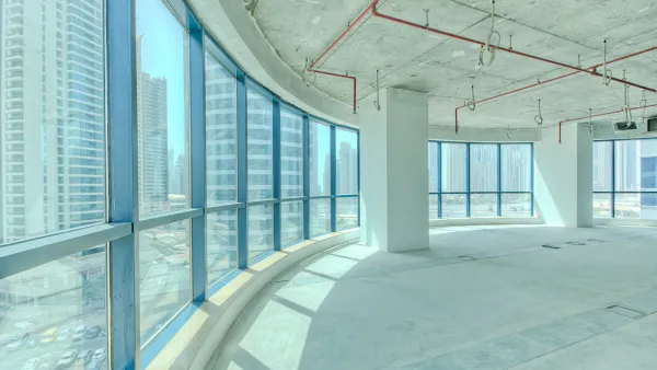 Curved window wall in vacant high-rise office building with light concrete floor and walls viewed from inside.