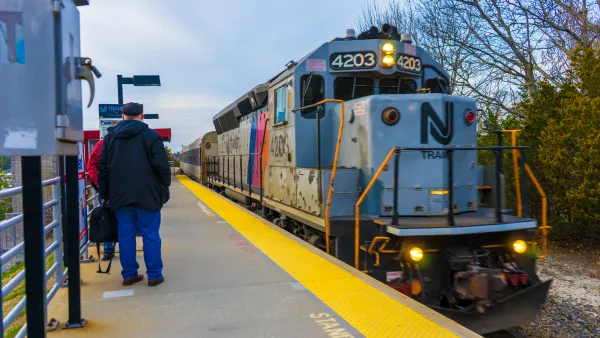 A New Jersey train approaches people waiting at the station.