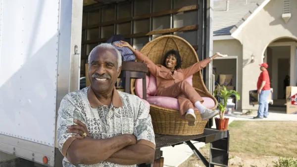 African American senior couple smiling in front of a moving truck in front of a single-family home.