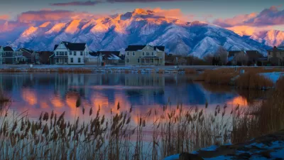 View of houses against backdrop of snowy mountains from across a lake at sunset or sunrise