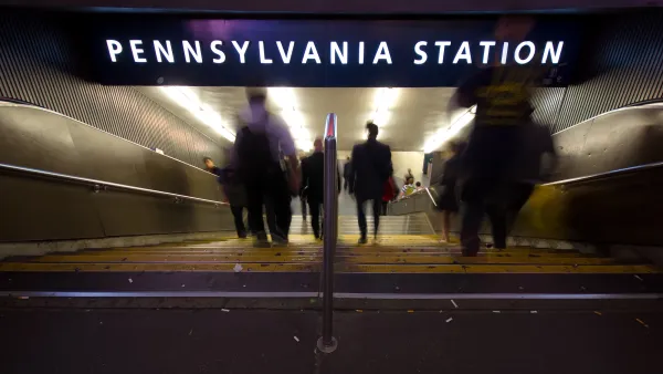 Blurred people in shoadow going down dark staircase under 'Pennsylvania Station' sign.