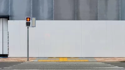 Crosswalk leading to sidewalk and blank construction wall with pedestrian crossing light