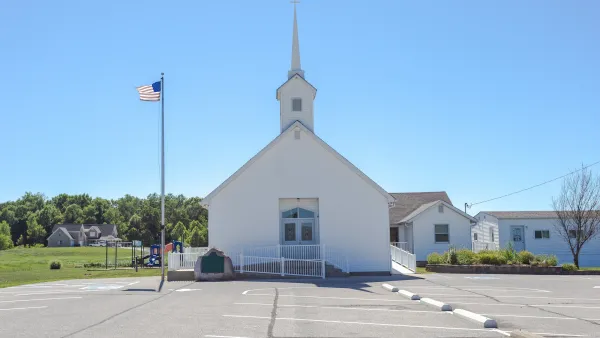 Small white church with steeple with asphalt parking lot in front.