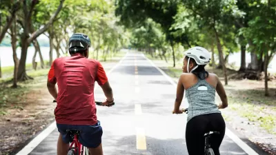 Two people riding bikes with helmets on paved park trail