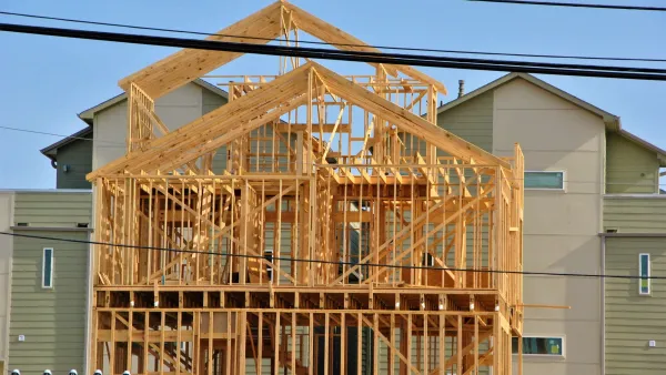 Wood-framed townhomes under construction in Houston, Texas with light green two-story building in background.