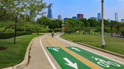 Paved two-way bike trail with yellow center line, green paint, and Chicago buildings inbackground