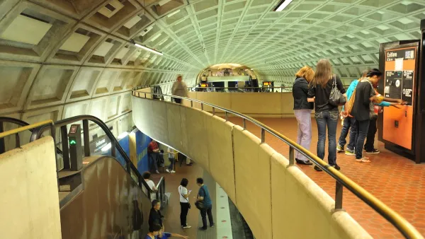 View from second-story level in Washington DC subway station with riders looking at maps and taking escalator down.