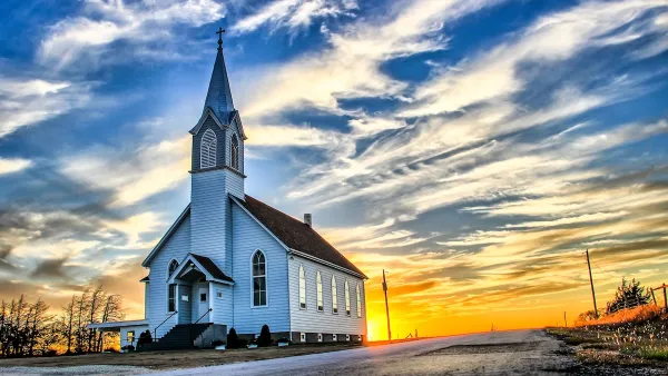 Rural white wooden church with tall steeple against sunset light in rural Kansas.