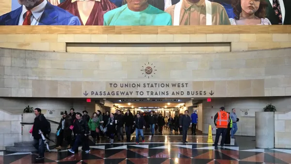 Crowd at entrance to pedestrian tunnel in Los Angeles Union Station with sign for trains and large mural above tunnel entrance. 
