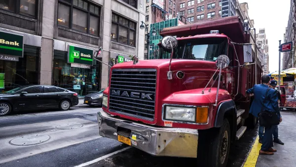 Large red freight truck parked curbside on street in New York City with two men in suits standing next to it.