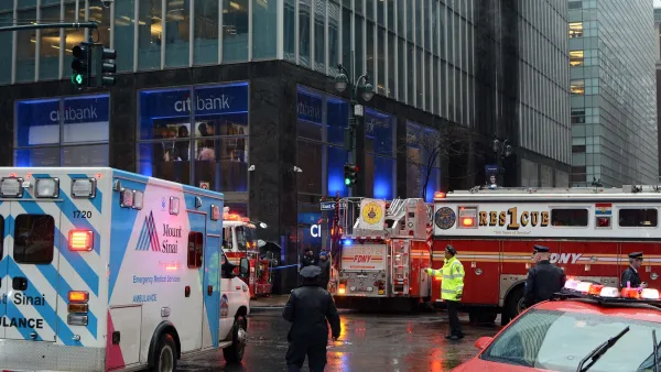 Fire truck, ambulance, and other emergency vehicles circled around a New York City intersection with police officer directing traffic in middle.