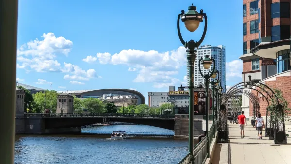 Two people walking on paved path next to river with vintage street lamps on a sunny day in Milwaukee, Wisconsin.