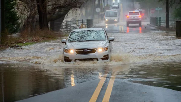 White car driving on flooded street.