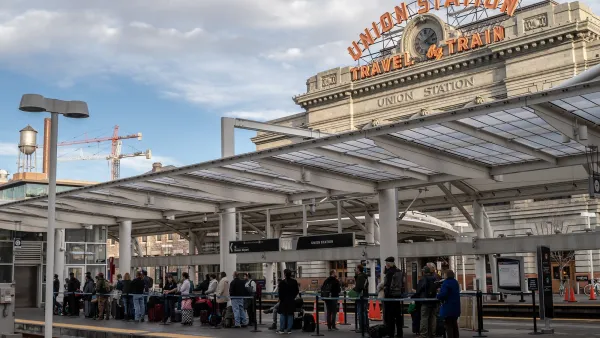 Line of passengers outdoors at Union Station in Denver, Colorado with vintage Union Station - Travel by Train sign in background.