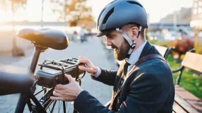 Young bearded man with helmet setting up battery on back of electric bike