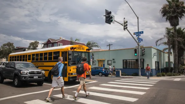 Two people with backpacks on crossing a crosswalk in front of a yellow school bus in San Diego, California.