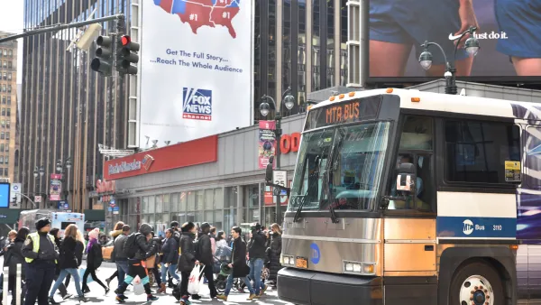 An MTA bus enters from the right side of the photo. To the left, people cross the street behind the bus.