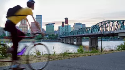 Cyclist on bike path in Portland, Oregon with bridge over river and city skyline in background.