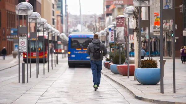 Man rides green share scooter on protected bus lane with blue bus in front of him in Denver, Colorado.
