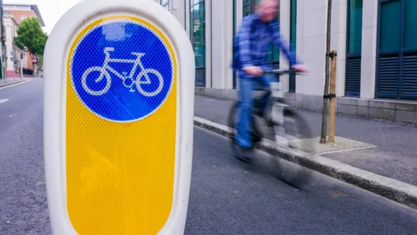 Close-up on plastic bollard with blue and white bike logo in bike lake in Ireland with blurred bike rider in background.