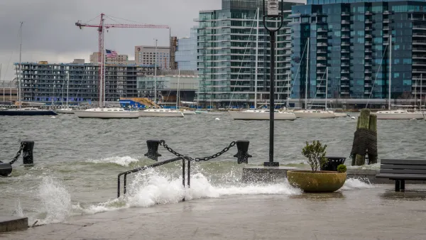 Waves splash over concrete dock in Boston harbor during a storm.