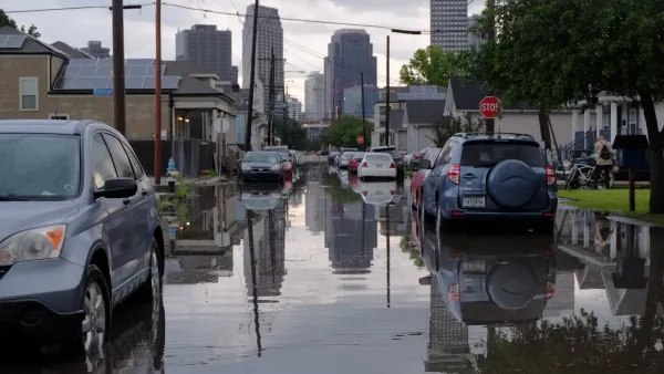Carsparked on flooded street in New Orleans with downtown high-rises visible in background.