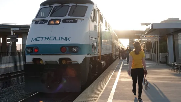 A woman in a yellow top walks down a train platform next to white Metrolink train in Anaheim, California.