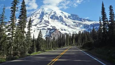 Two-lane asphalt road in Washington state with pine trees along sides and Mt. Rainier in background