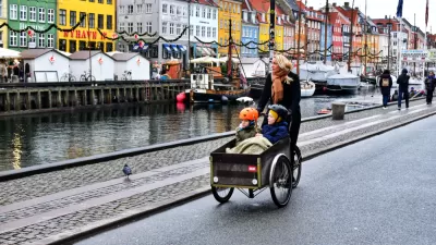 Woman riding cargo bike with two small children on Copenhagen street next to a canal