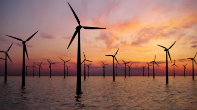 Offshore wind turbines in water against a sunset sky