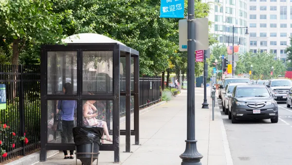 A bus stops with local commuters waiting for their buses in Boston, Massachusetts. There are trees behind the bus shelter.