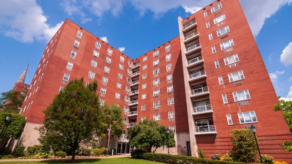 Multistory red apartment building in Pittsburgh, PA against blue sky with white clouds.
