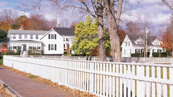 White picket fence along street with white two-story houses in the background in Wicasset, Maine.