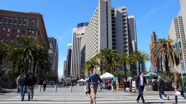 People cross a wide street in San Francisco, with tall buildings in the background.
