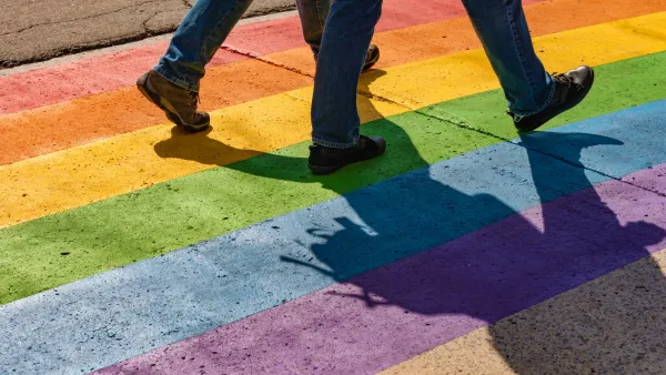 Close-up on legs of two people walking on rainbow-painted crosswalk.