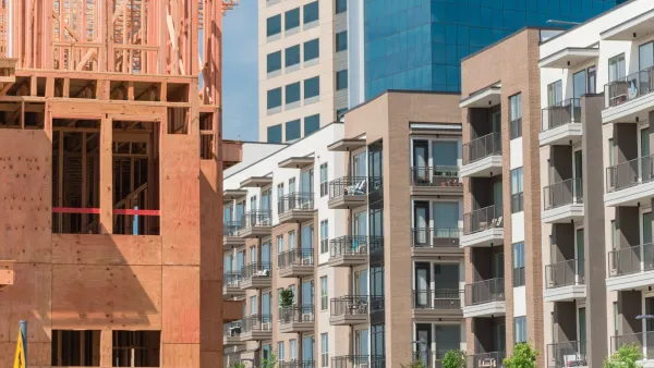 Incomplete wood-frame apartment building in foreground with completed apartment building in background.