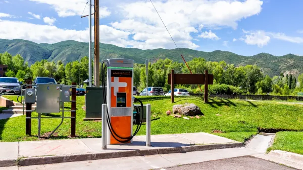 Orange EV charger in outdoor parking lot with Colorado mountains in background on sunny day.