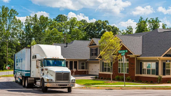 Large white moving truck pulling away from brick suburban single-family homes in Atlanta, Georgia.