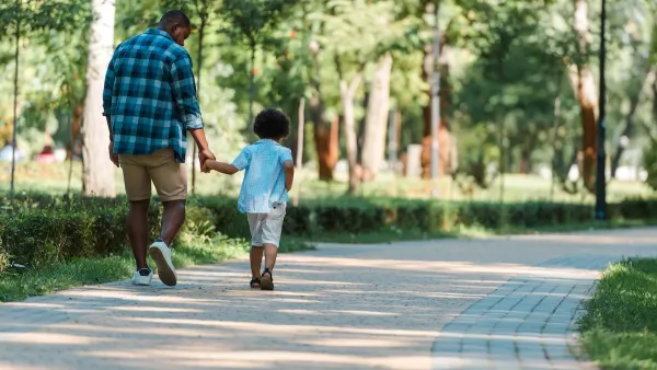 Dad and toddler holding hands walking down path in park.
