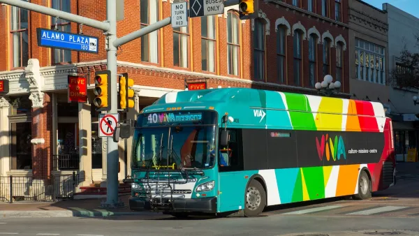A colorful Via transit bus next to a brick building.