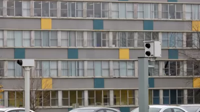 Two white traffic enforcement cameras above a road in Ottawa, Canada with a colorful multistory building in background