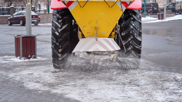 Yellow truck dropping salt onto a snowy road.