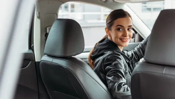 Young woman driver in black leather jacket looking back at passenger seat.